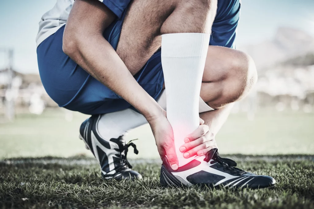 Injury, sports and hand of a man on foot pain, soccer emergency and accident while training. Fitness, problem and an athlete or football player with inflammation or a swollen muscle on the field.